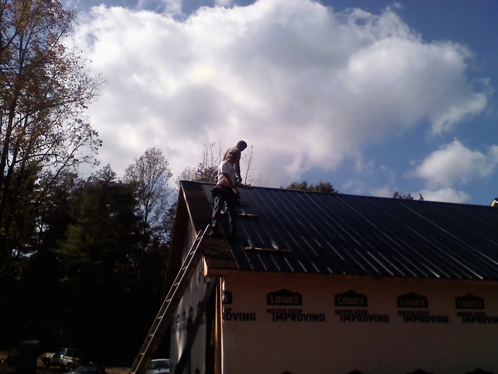 Roofer fastening dark metal panels high against a cloudy sky, from a Roof Inspection job in Norwood